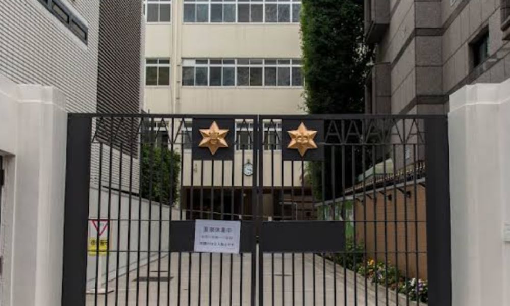 麻布中学校・麻布高校の校門。白い壁と金色の校章が付いた黒い鉄門が写っている