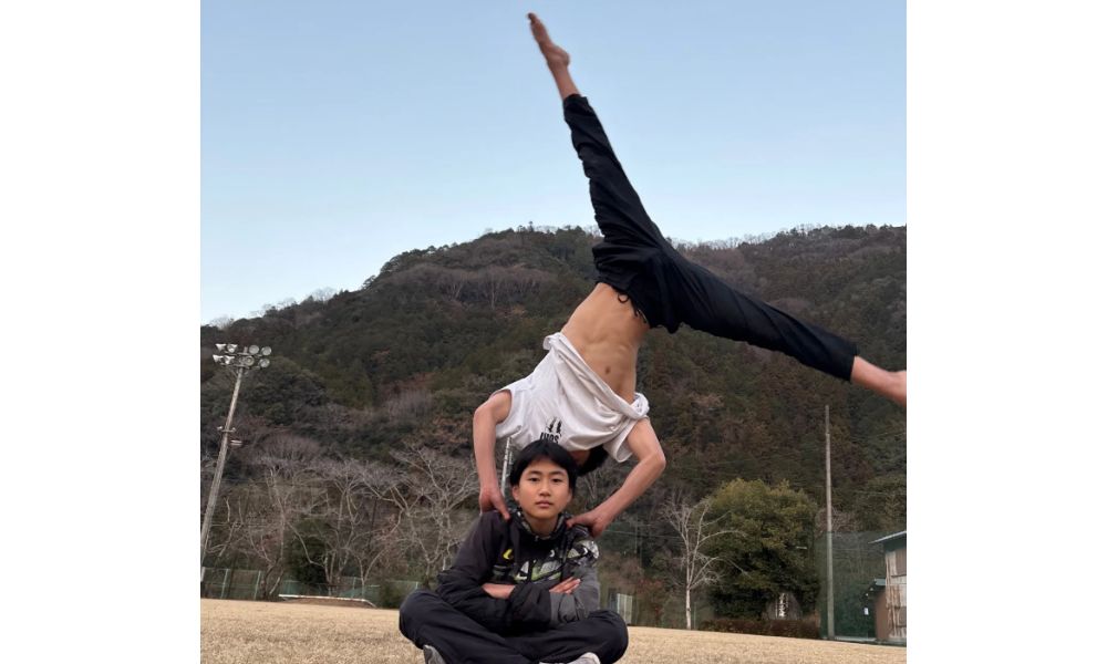 廣川家の長男・和楽くんがグラウンドで座っている後ろで、相手が片手倒立のようなアクロバットを決めるサーカス学校での練習風景