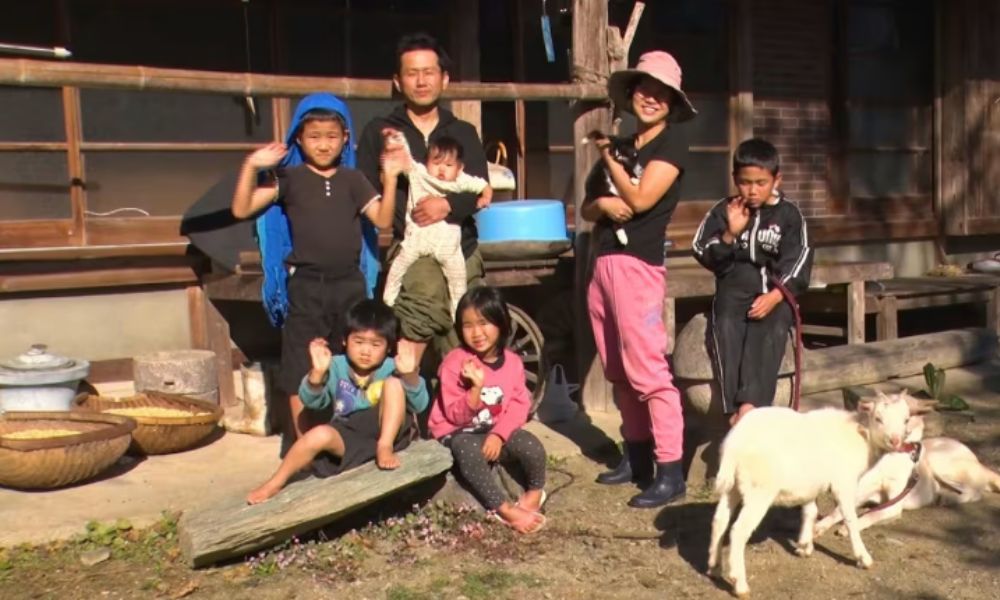 徳島で自給自足生活を送る大家族・廣川家の集合写真。両親と子どもたち、ヤギが古民家の前に集まっている