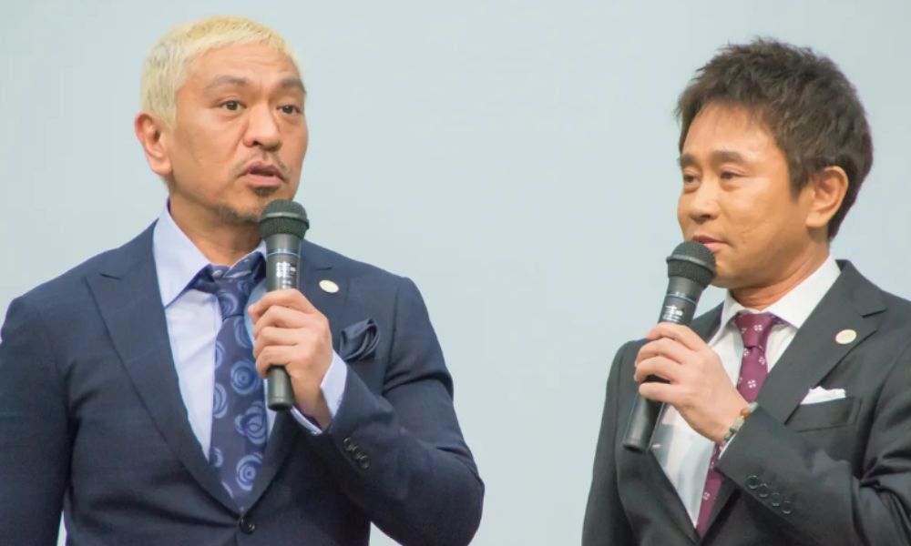 スーツ姿でマイクを持ち話すお笑いコンビ・ダウンタウンの松本人志と浜田雅功