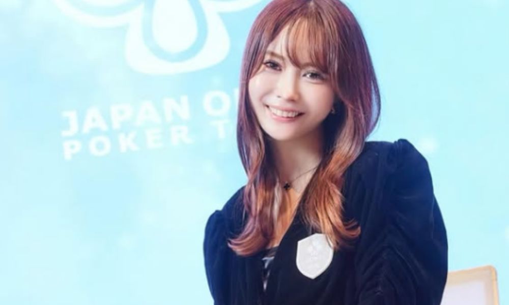 JAPAN OPEN POKER TOURの背景を前に笑顔を見せるプロポーカープレイヤー・岡本詩菜のポートレート