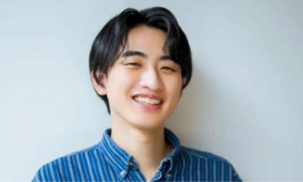 春とヒコーキ・土岡哲朗のポートレート写真。笑顔で青いストライプシャツを着たお笑い芸人