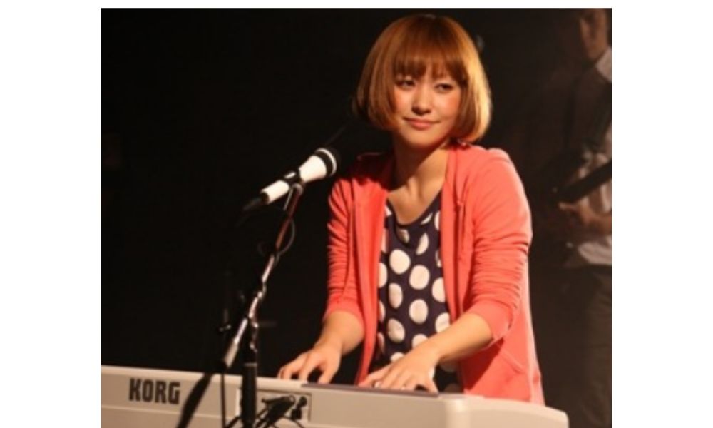 近藤夏子がステージで白いKORGキーボードを弾き語りするライブパフォーマンスの様子