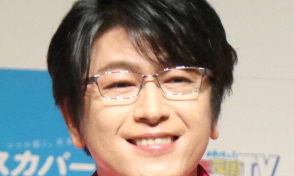 及川光博(ミッチー)が銀縁の眼鏡をかけて満面の笑みを浮かべる近影。ピンクのラメ入りジャケット姿でイベント・テレビ出演時の写真