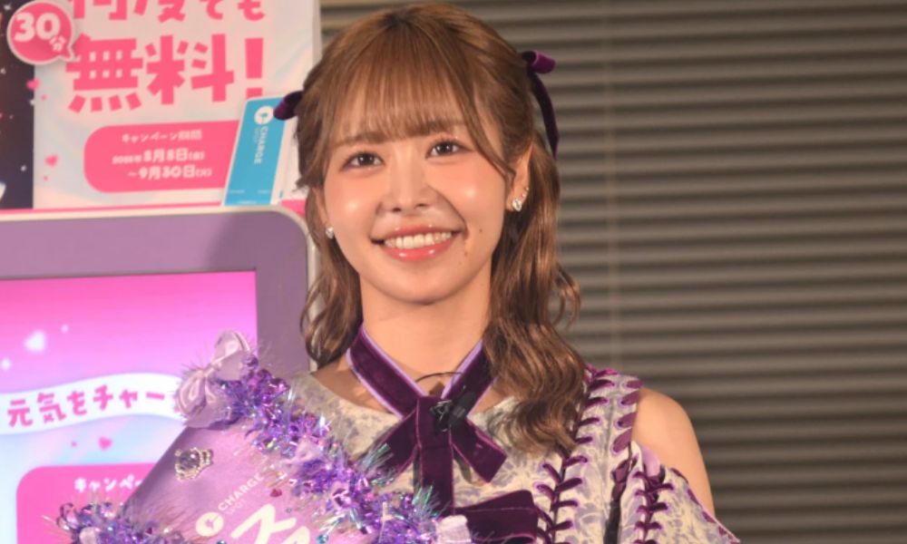 FRUITS ZIPPER仲川瑠夏（るなぴ）が紫色のリボン付きステージ衣装で笑顔を見せるイベントショット。ChargeSPOTキャンペーン発表会での様子